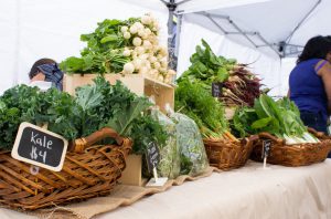 Veggies in crates sit atop a table underneath a market tent
